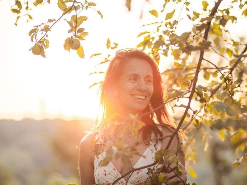 Porträt einer lächelnden, selbstbewussten Frau, die an einem Apfelbaum steht